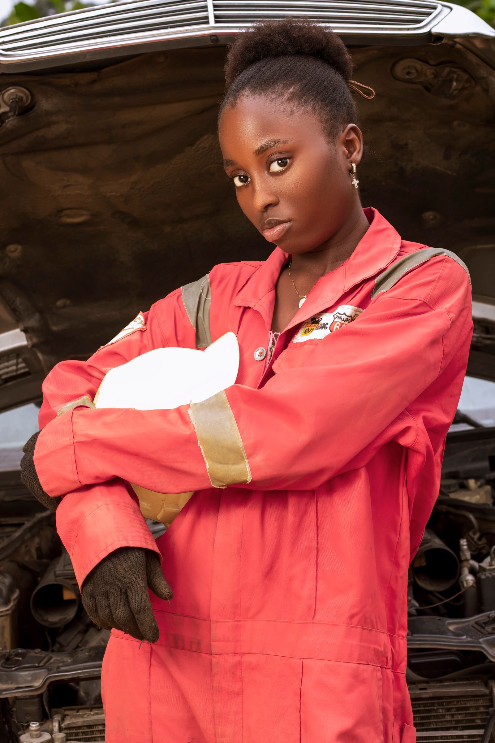 A confident woman mechanic standing in front of an open vehicle hood in a workshop